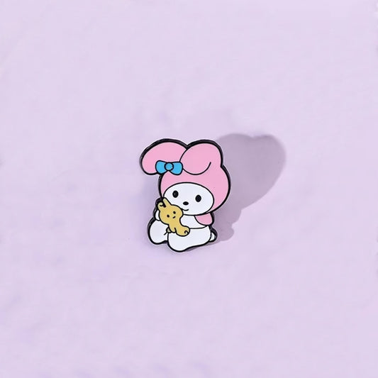 un pin's au design du personnage My Melody de Sanrio. Identifiable grâce à ses longues oreilles roses, il est ici dans une pose trop mignonne avec un petit ourson en peluche dans les mains.
