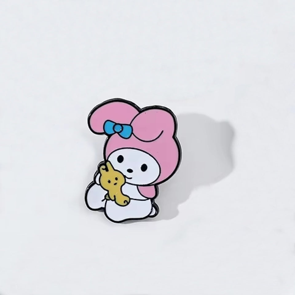 un pin's au design du personnage My Melody de Sanrio. Identifiable grâce à ses longues oreilles roses, il est ici dans une pose trop mignonne avec un petit ourson en peluche dans les mains.