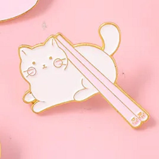 un adorable pin's en forme de chat blanc sur lequel repose une paire de baguettes au motif de patte de chat.