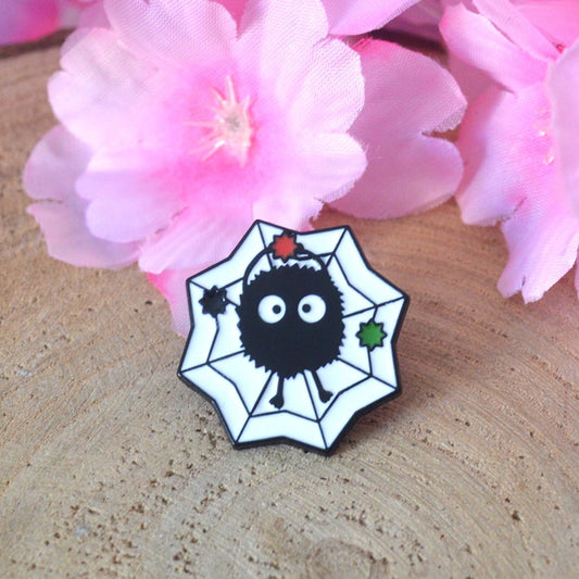 un pin's en forme de noiraude tiér des films Ghibli : le voyage de Chihiro et Mon voisin Totoro. La noriaude lève un morceau de sucre et elle est sur un fond en forme de toile.
