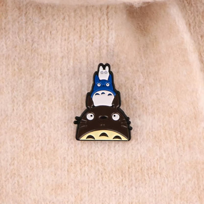 un pin's inspiré de Totoro et de ses amis. Sur la tête du gros Totoro se trouve le chibi bleu puis le chibi blanc, empilé les uns sur les autres