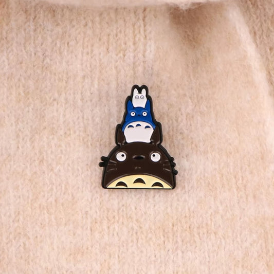 un pin's inspiré de Totoro et de ses amis. Sur la tête du gros Totoro se trouve le chibi bleu puis le chibi blanc, empilé les uns sur les autres