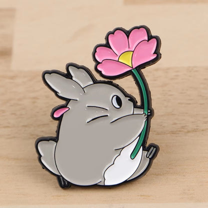 un pin's représentant Totoro qui tient une grosse fleur rose dans ses pattes