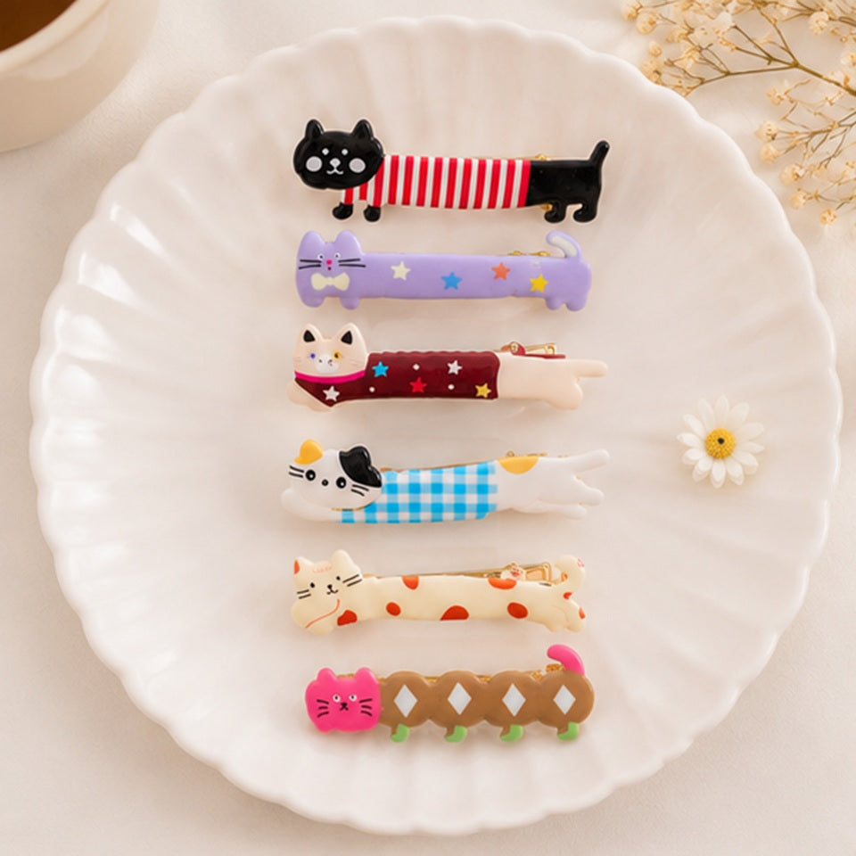 Lot de pinces à cheveux kawaii en forme de chats allongés colorés présenté sur une jolie assiette blanche ✨ Accessoires adorables avec motifs chats, étoiles, rayures et carreaux pastel, parfaits pour ajouter une touche cute, originale et amusante à une coiffure. Ambiance douce et élégante inspirée de l’univers kawaii japonais.