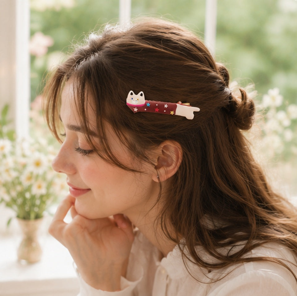 Personne portant une pince à cheveux kawaii en forme de chat allongé avec étoiles colorées ✨ Accessoire adorable et original parfait pour ajouter une touche cute et fantaisie à une coiffure. Ambiance douce et lumineuse avec fleurs et décoration cosy inspirée de l’univers kawaii japonais.
