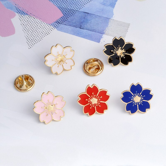 des pin's en forme de fleur de sakura colorée : noir, rouge, bleu, blanc et rose. Avec leur finition dorée, ils sont symbole de renouveau et de beauté.