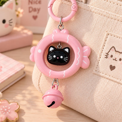 Porte-clés kawaii rose en forme de poisson avec petit chat noir et grelot, accroché à un sac beige dans un décor pastel mignon et fleuri.