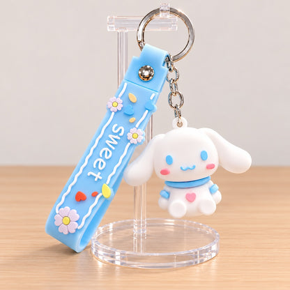 Porte-clés kawaii Cinnamoroll Sanrio avec adorable figurine blanche aux longues oreilles, joues roses et détails bleu pastel. Accompagné d'une dragonne bleue décorée de petites fleurs, de cœurs colorés et de l'inscription « Sweet », ce porte-clés mignon est présenté sur un support transparent, dans un décor pastel. Accessoire kawaii idéal pour personnaliser ses clés, son sac à main ou son sac à dos, et une jolie idée cadeau pour les fans de Cinnamoroll et de l'univers Sanrio.
