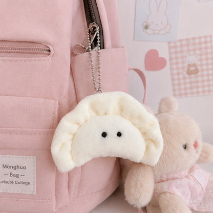 un porte-clés peluche en forme de gyoza blanc crème avec de petits yeux noirs brodé suspendu à un sac rose grâce à une chaîne argentée à billes. Ambiance chaleureuse et mignonne, féminine et kawaii.