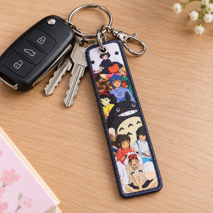 Porte-clé rectangulaire Studio Ghibli avec Totoro, Chihiro, Kiki et Princesse Mononoké, accroché à un trousseau de clés de voiture et de maison, sur un bureau en bois clair.