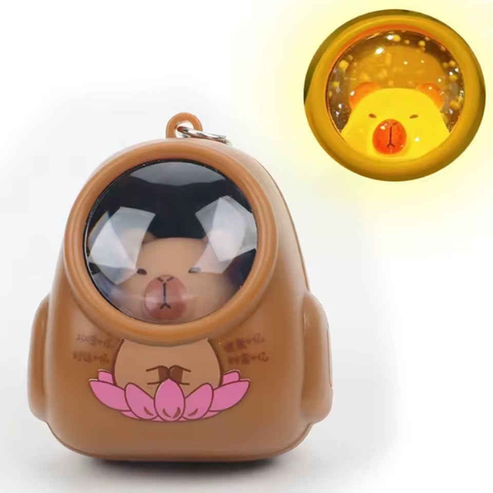 un porte-clé lumineux en forme d'un capybara portant une combinaison. Quand on l'allume, les étoiles et la galaxie apparaissent dans son casque.