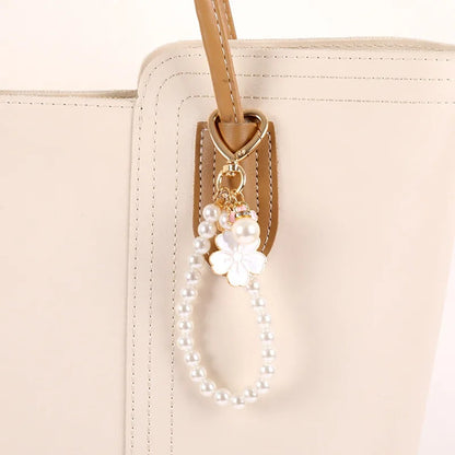 Porte-clé bijou avec perles blanches, mousqueton cœur doré et pendentifs fleurs de sakura roses accroché sur une anse d'un sac à main.