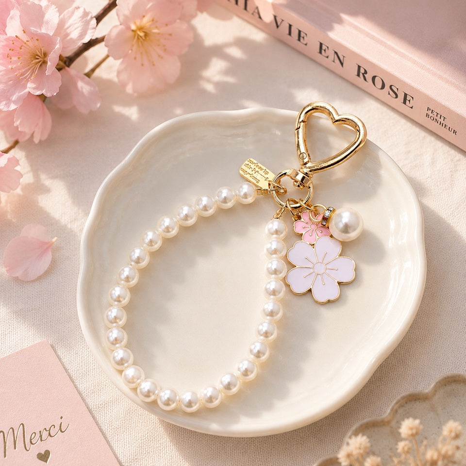 Porte-clé bijou avec perles blanches, mousqueton cœur doré et pendentifs fleurs de sakura roses, présenté dans un décor pastel élégant et fleuri.