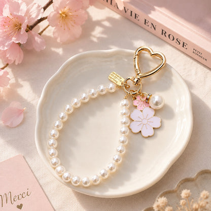 Porte-clé bijou avec perles blanches, mousqueton cœur doré et pendentifs fleurs de sakura roses, présenté dans un décor pastel élégant et fleuri.