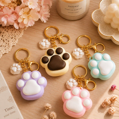 Porte-clés kawaii en forme de grosses pattes de chat colorées rose, violet, bleu et beige, avec mousquetons dorés et mini pattes assorties, présentés sur une jolie table décorée.