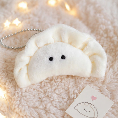 Porte-clés peluche kawaii en forme de gyoza  mignon blanc crème est présenté sur un tapis beige. L'ambiance douce et chaleureuse est agrémentée d'une guirlande lumineuse et d'éléments décoratifs inspirés de l'univers kawaii japonais. Idéal pour personnaliser un sac, un sac à dos ou un trousseau de clés.
