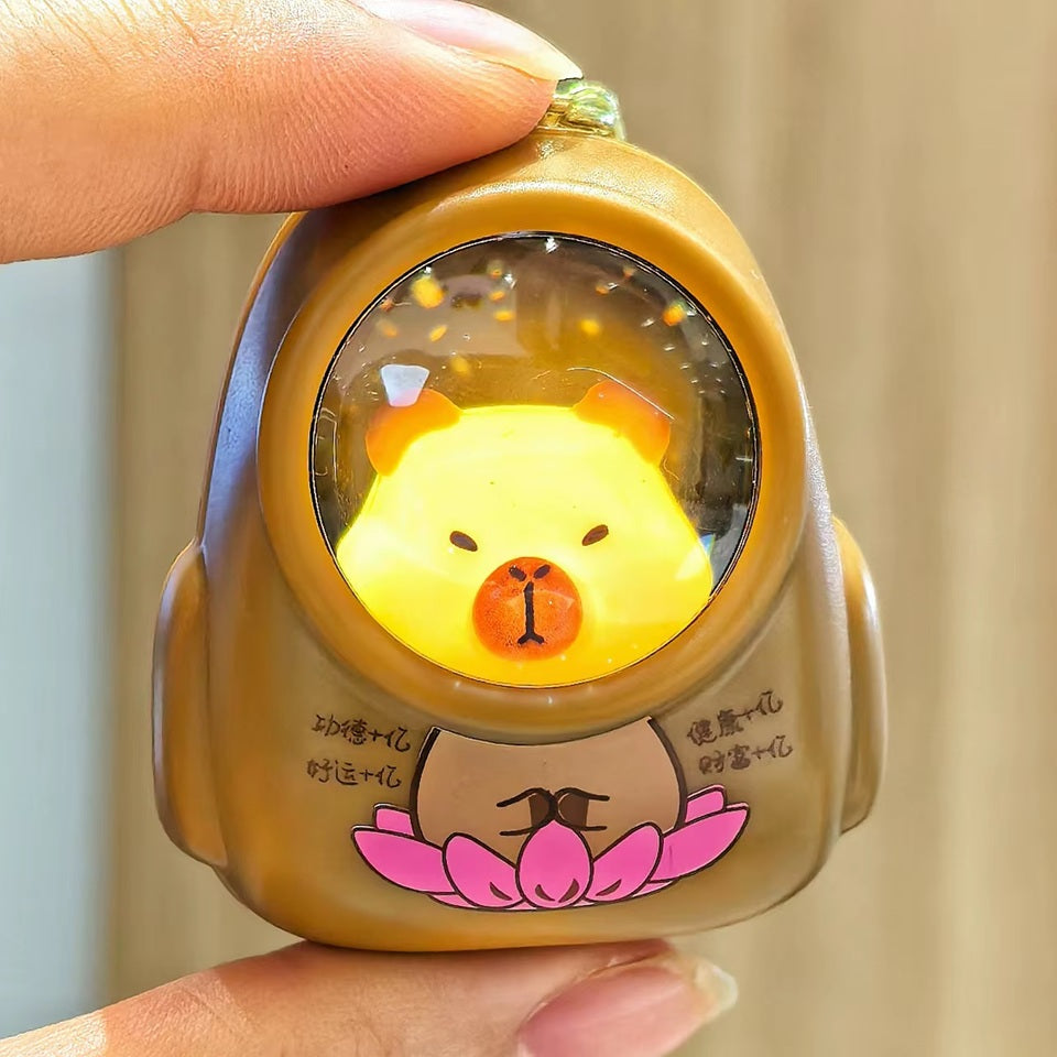un porte-clé lumineux en forme d'un capybara portant une combinaison. Quand on l'allume, les étoiles et la galaxie apparaissent dans son casque.
