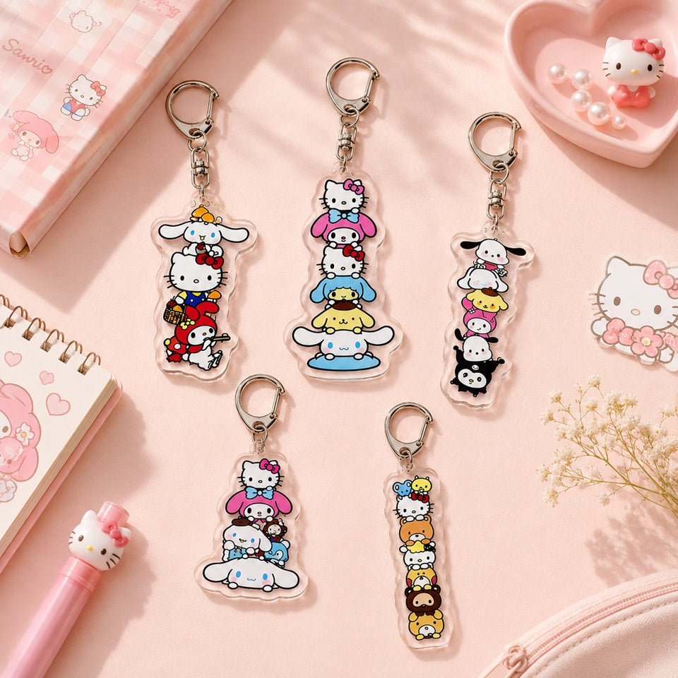 Cinq porte-clés en acrylique transparent représentant différents assemblages de personnages de la famille Sanrio, dont Hello Kitty, Cinnamoroll, My Melody, Kuromi, Pompompurin et leurs amis. Les cinq modèles sont entièrement visibles et disposés à des positions variées sur un fond rose pastel, entourés de petites décorations kawaii. L'ensemble crée une présentation lumineuse, douce et élégante.