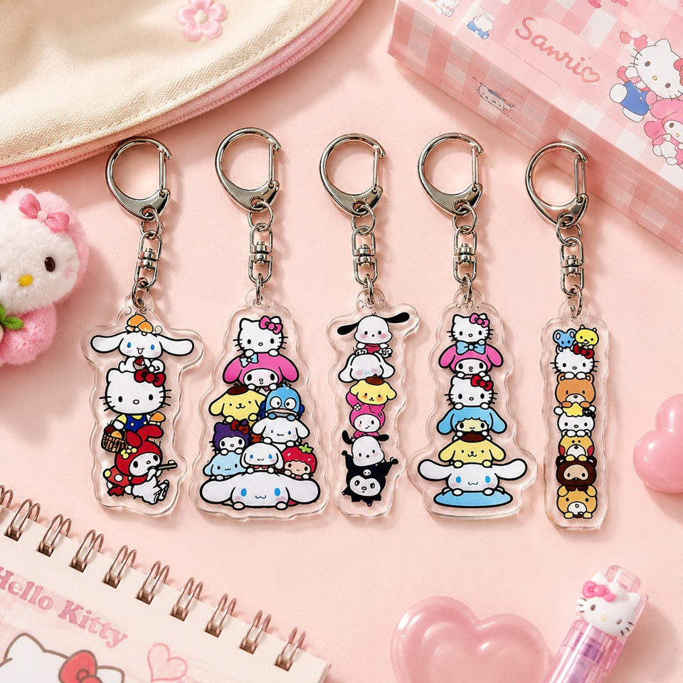 Porte-clés en acrylique transparent représentant plusieurs personnages emblématiques de la famille Sanrio, dont Hello Kitty, Cinnamoroll, My Melody, Kuromi, Pompompurin et d'autres compagnons. Les cinq modèles sont alignés sur un fond rose pastel avec un carnet, une trousse et des accessoires assortis, créant une ambiance kawaii douce et colorée.