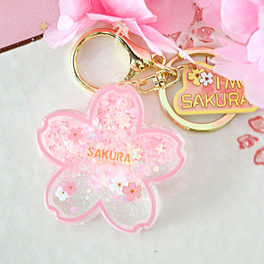 un porte-clés en forme de fleur de sakura rose dans lequel se trouve des paillettes en forme de fleurs façon quicksand. L'ensemble est poétique et magique.