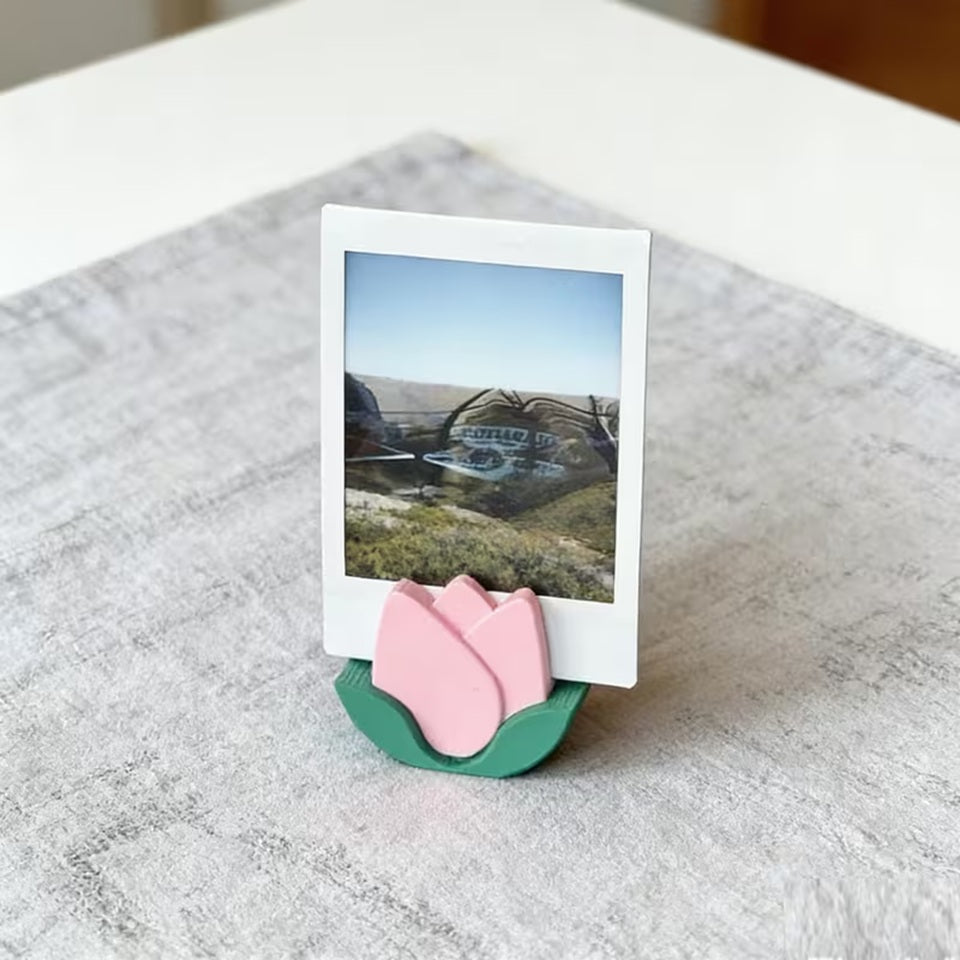 un porte-photo en forme de tulipe rose dans lequel est posé une photo. L'ambiance est douce et calme. Idéal pour une touche décoration florale mignonne
