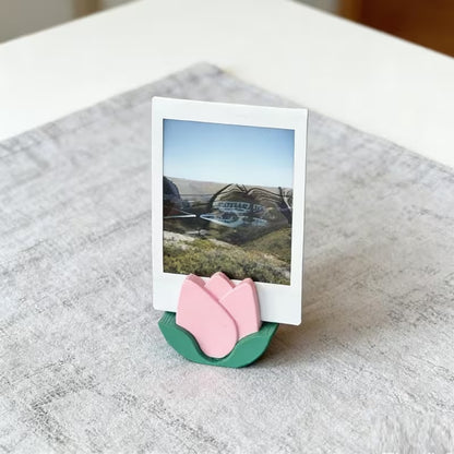 un porte-photo en forme de tulipe rose dans lequel est posé une photo. L'ambiance est douce et calme. Idéal pour une touche décoration florale mignonne