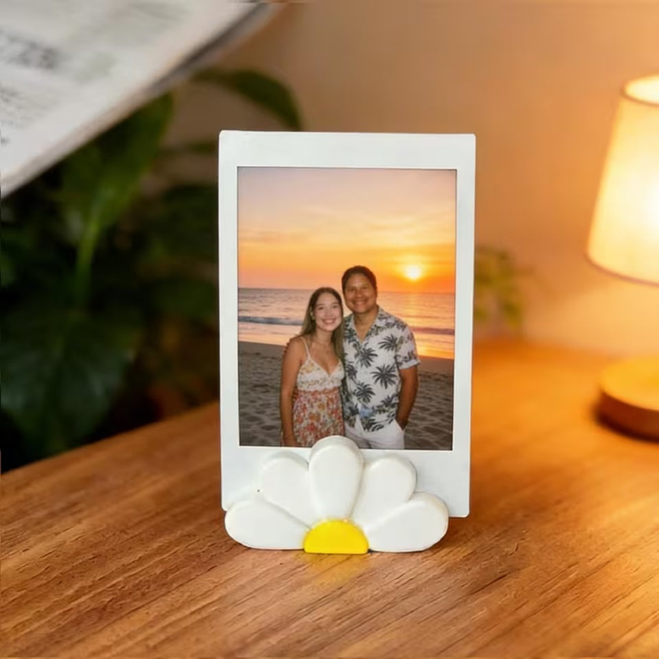un porte-photo en forme de marguerite dans lequel est posé une photo d'un couple au coucher de soleil. LA lumière d ela pièce est douce et chaude. Idéal pour une touche décoration florale mignonne