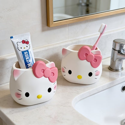 deux pots à crayons en forme d'Hello Kitty, posés sur le rebor d'un lavabo dans une salle de bain blanche et lumineuse. Un dentifrice et une brosse à dent y sont posés à l'intérieur.