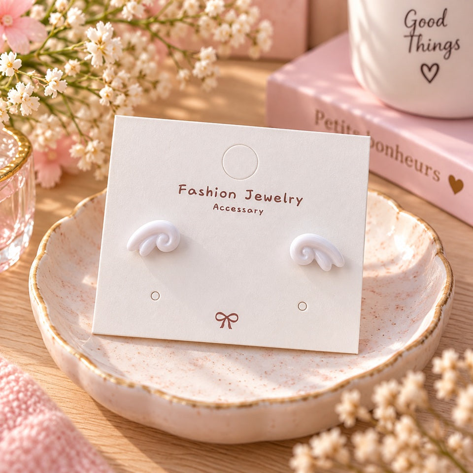 Puces d’oreilles blanches au design tourbillon, présentées sur un support à bijoux dans un décor romantique rose et fleuri.