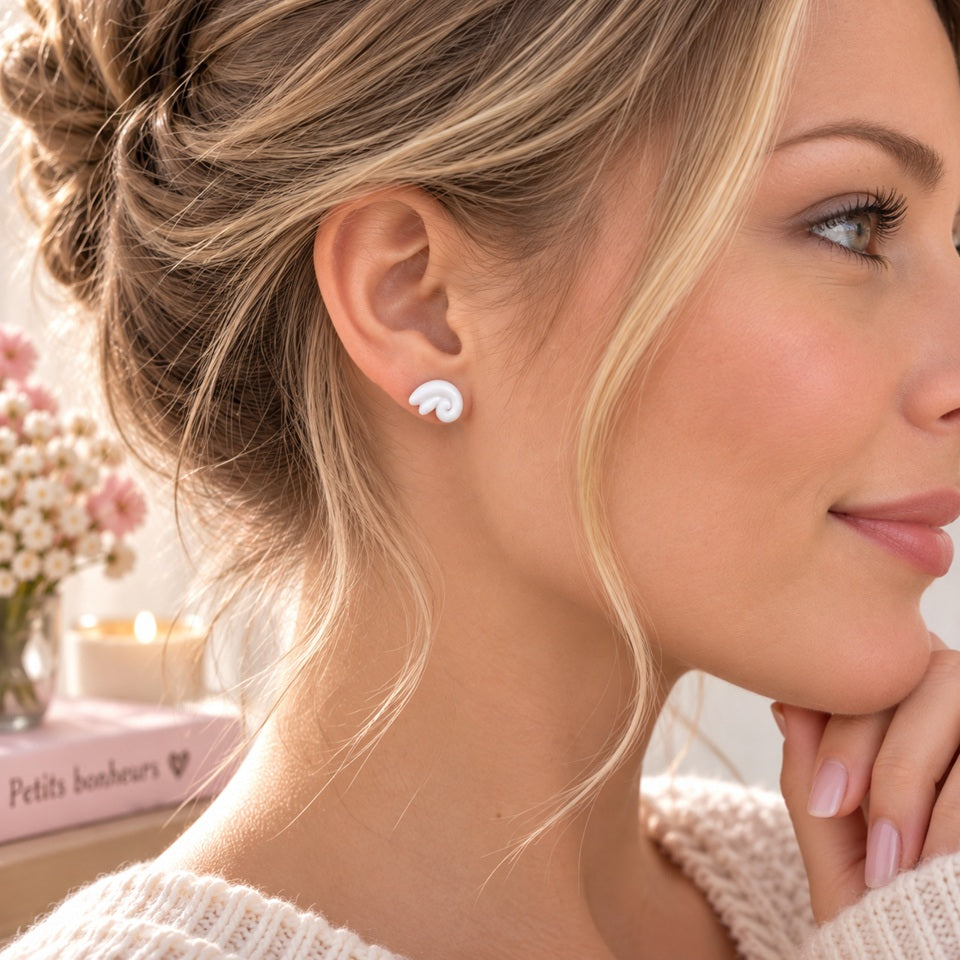 Petite puce d’oreille blanche au design tourbillon portée par une femme de profil, bijou discret et tendance au style féminin.