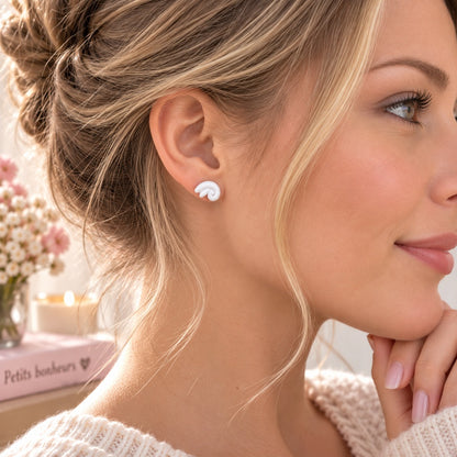 Petite puce d’oreille blanche au design tourbillon portée par une femme de profil, bijou discret et tendance au style féminin.