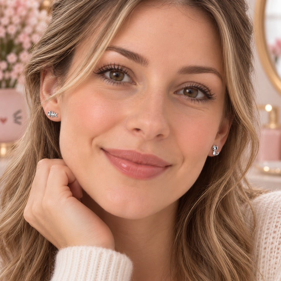 Femme portant des puces d’oreilles asymétriques argentées en forme de chat et d’arête de poisson, petits bijoux kawaii délicatement posés sur les lobes.
