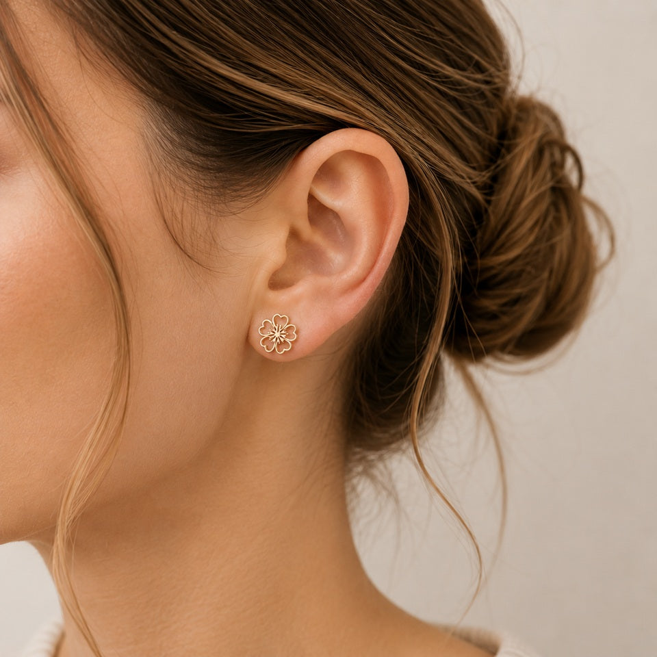 une paire de puces d'oreilles dorées en forme de fleur de sakura dans un style minimaliste et mignon