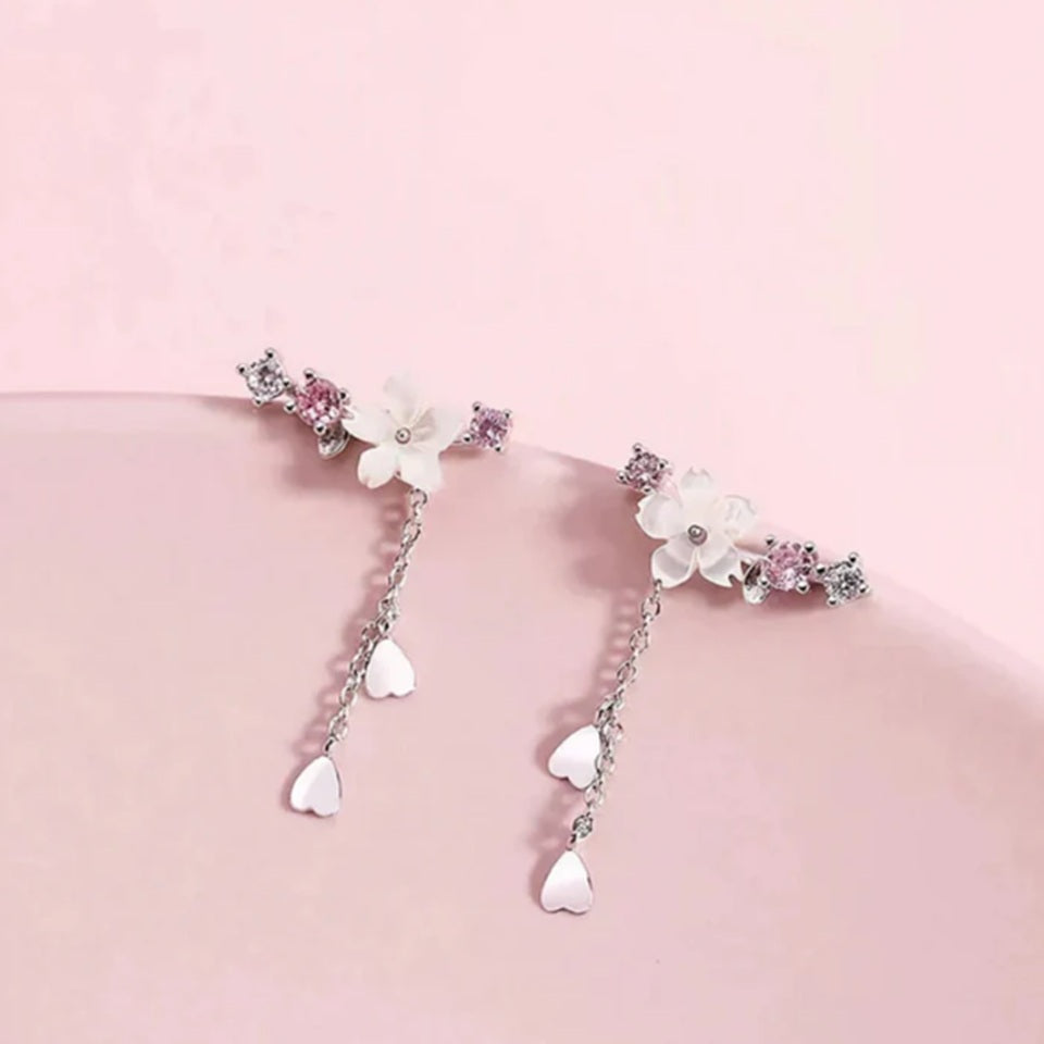 une paire de boucles d'oreilles qui épousent le lobe de l'oreille avec délicatesse et élégance. Une jolie fleur de sakura blanche et des strass blancs et roses viennent embellir l'ensemble. ne petite chaine pendante ornée de pétale de sakura est suspendue aux boucles.