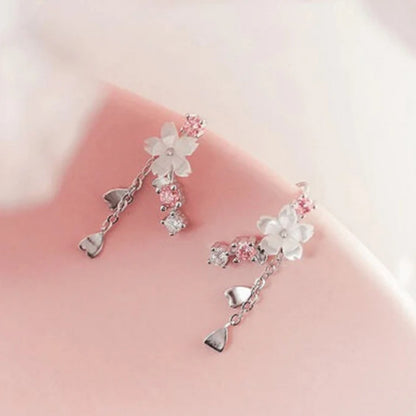 une paire de boucles d'oreilles qui épousent le lobe de l'oreille avec délicatesse et élégance. Une jolie fleur de sakura blanche et des strass blancs et roses viennent embellir l'ensemble. ne petite chaine pendante ornée de pétale de sakura est suspendue aux boucles.