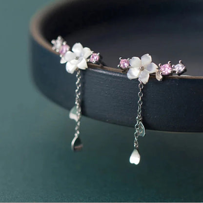 une paire de boucles d'oreilles qui épousent le lobe de l'oreille avec délicatesse et élégance. Une jolie fleur de sakura blanche et des strass blancs et roses viennent embellir l'ensemble. ne petite chaine pendante ornée de pétale de sakura est suspendue aux boucles.