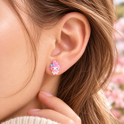 Petite puce d’oreille My Melody rose kawaii portée à l’oreille, avec personnage entier et nœud bleu, dans un décor doux et fleuri.