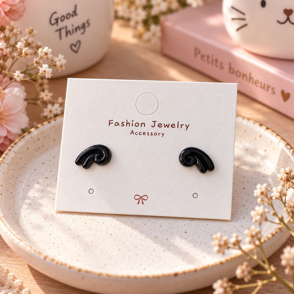 Puces d’oreilles noires au design tourbillon, présentées sur un support à bijoux dans un décor féminin doux et fleuri.