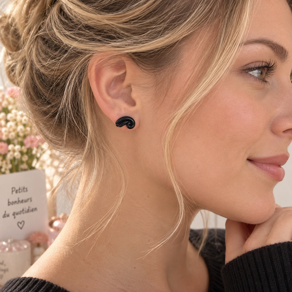 Puce d’oreille noire au design tourbillon portée par une femme de profil, un bijou original et tendance au style moderne.
