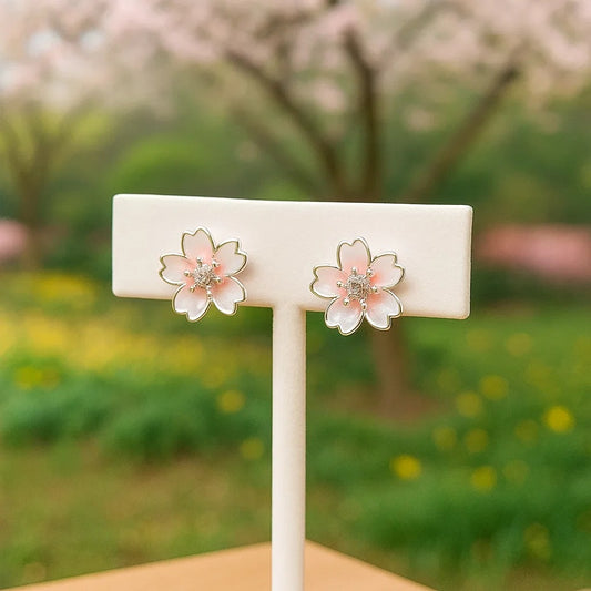 Une paire de puces d'oreilles argentées  délicates en forme de fleurs de cerisier dont le coeur est un petit strass brillant. Leur coloris rosé est délicate