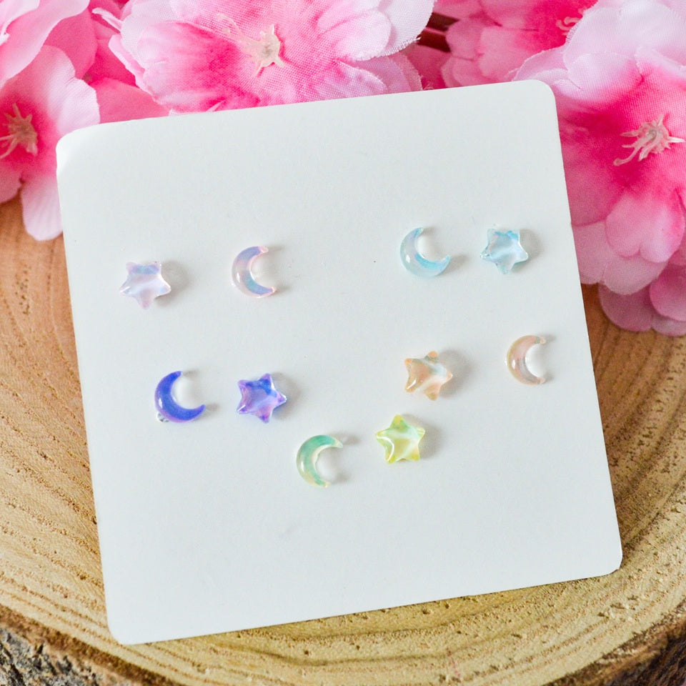 des puces d'oreilles asymétriques : un côté en forme de lune, un côté en forme d'étoile. Design minimaliste et coloré