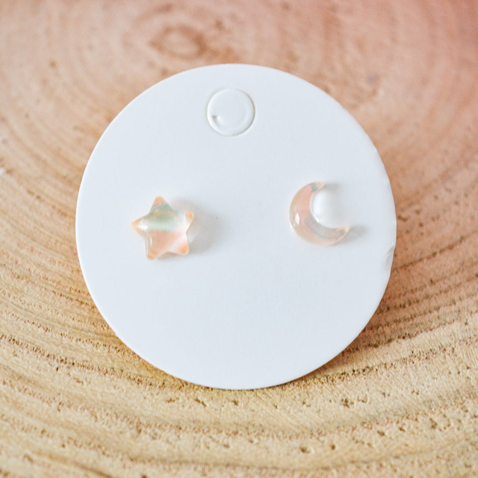 des puces d'oreilles asymétriques : un côté en forme de lune, un côté en forme d'étoile. Design minimaliste et coloré