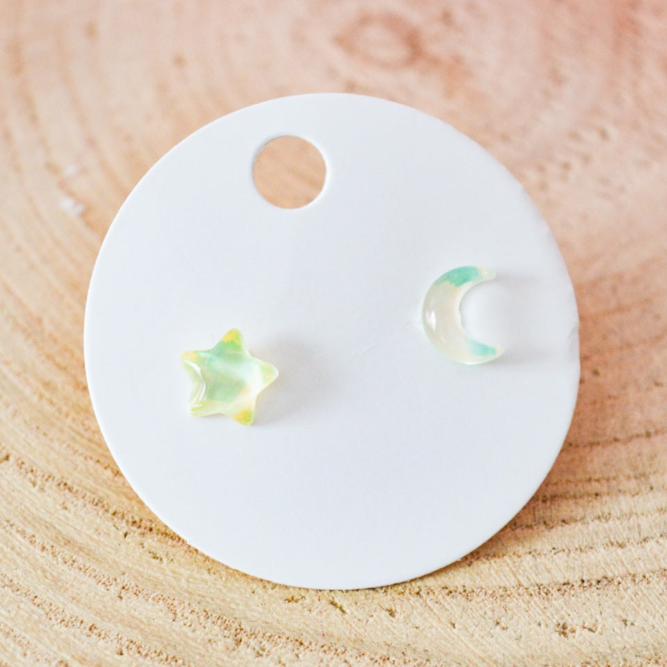 des puces d'oreilles asymétriques : un côté en forme de lune, un côté en forme d'étoile. Design minimaliste et coloré
