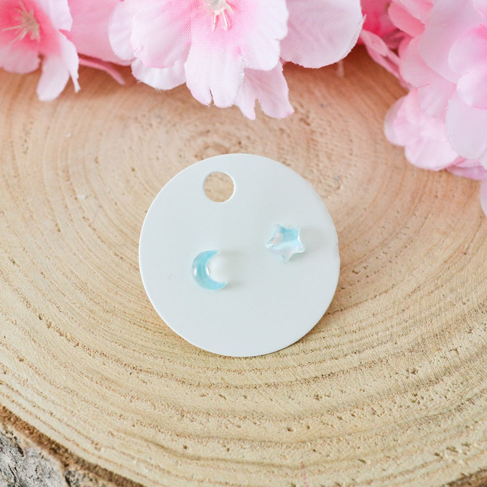 des puces d'oreilles asymétriques : un côté en forme de lune, un côté en forme d'étoile. Design minimaliste et coloré