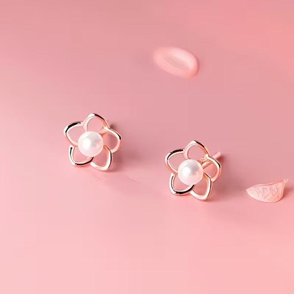 des puces d'oreilles en forme de petites fleurs dorées dont le coeur est une perle blanche. Le style est minimaliste et élégant.