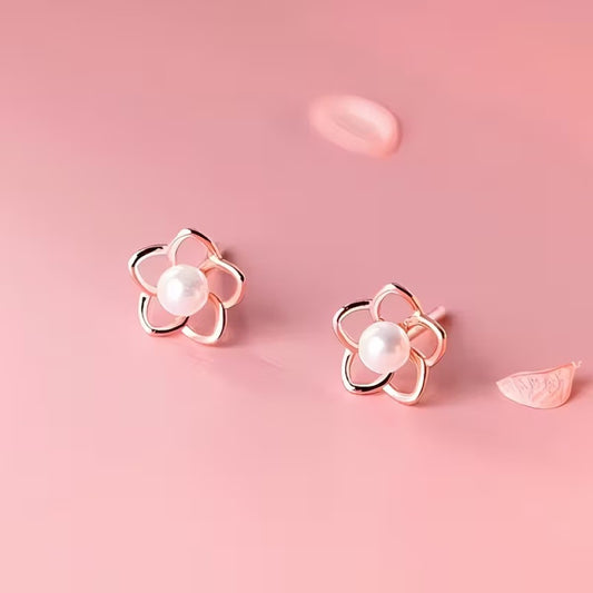 des puces d'oreilles en forme de petites fleurs dorées dont le coeur est une perle blanche. Le style est minimaliste et élégant.