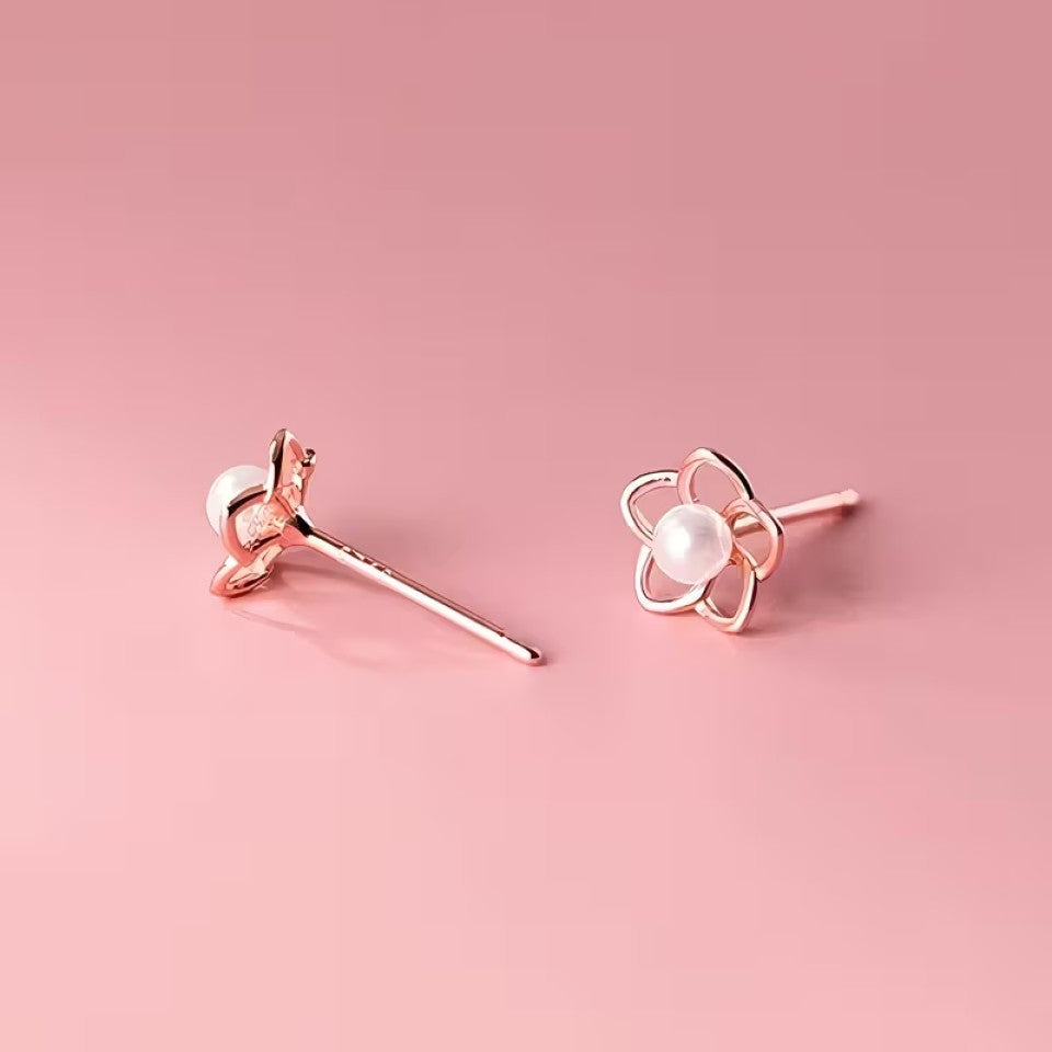 des puces d'oreilles en forme de petites fleurs dorées dont le coeur est une perle blanche. Le style est minimaliste et élégant.