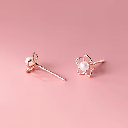 des puces d'oreilles en forme de petites fleurs dorées dont le coeur est une perle blanche. Le style est minimaliste et élégant.