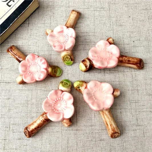 un repose baguette en céramique en forme d'une branche de cerisier sur laquelle est posé une délicate fleur de sakura rose. Idéal pour embellir et décorer une table