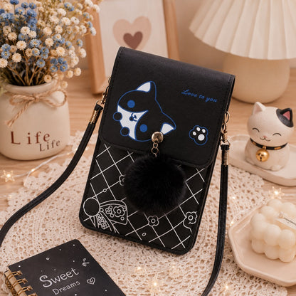 Sacoche téléphone noire kawaii avec motif chat, pompon noir et bandoulière, présentée dans un décor chaleureux et élégant avec fleurs séchées, lampe, figurine de chat, bougie et accessoires déco. Petit sac à bandoulière pour femme, pratique, compact et tendance.